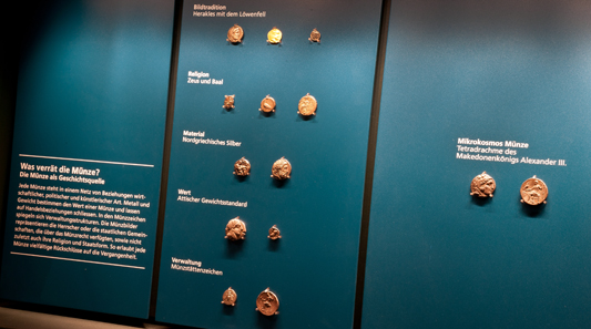 Teilansicht der Vitrine über die Aussagemöglichkeiten von Münzen, veranschaulicht am Beispiel der Tetradrachme Alexanders des Großen.